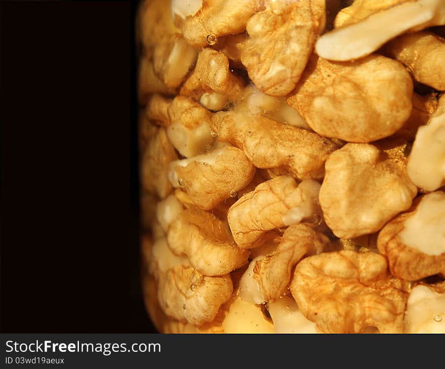 Walnut pieces and honey in a jar against black. Walnut pieces and honey in a jar against black