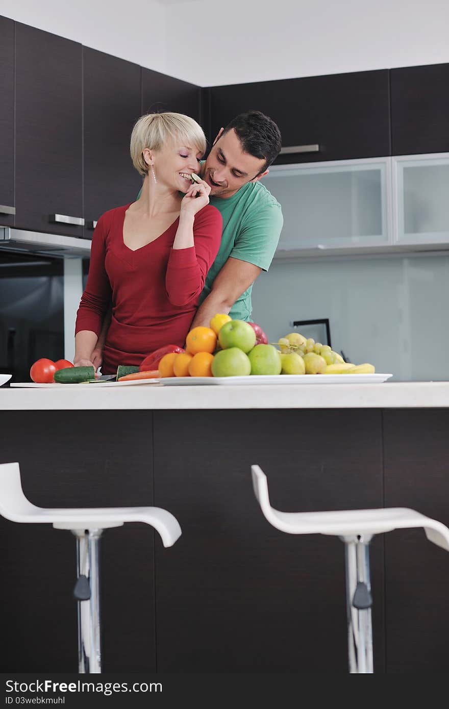 Happy young couple have fun in modern kitchen indoor while preparing fresh fruits and vegetables food salad