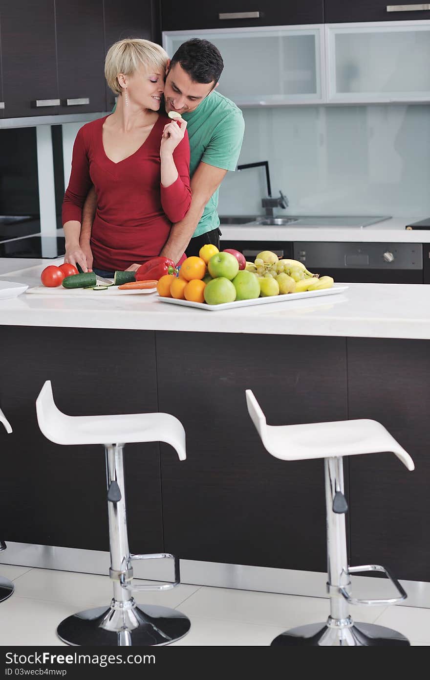 Happy young couple have fun in modern kitchen indoor while preparing fresh fruits and vegetables food salad