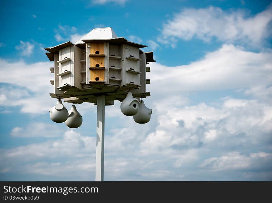 A wooden bird condo (large bird house) set against a cloudy blue sky. A wooden bird condo (large bird house) set against a cloudy blue sky.