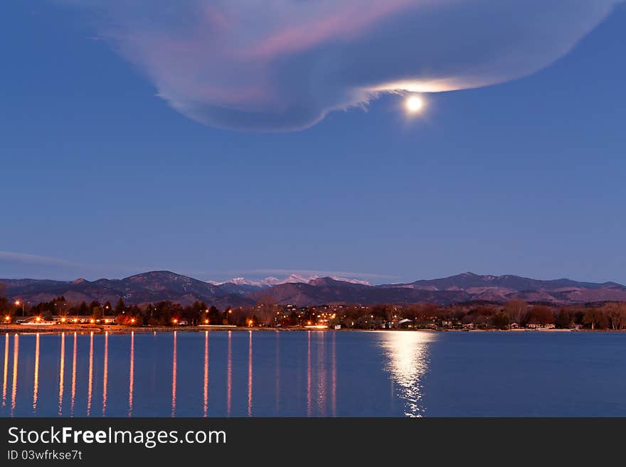 Full moon over urban lake at dawn, with snow capped mountains, light reflections and interesting cloud formation. Full moon over urban lake at dawn, with snow capped mountains, light reflections and interesting cloud formation.