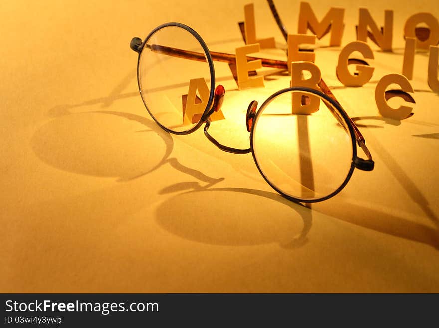 Reading concept. Old spectacles on yellow paper surface with cutting letters. Reading concept. Old spectacles on yellow paper surface with cutting letters