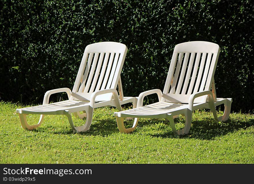 Two white lawn chairs in a green garden by summer. Two white lawn chairs in a green garden by summer