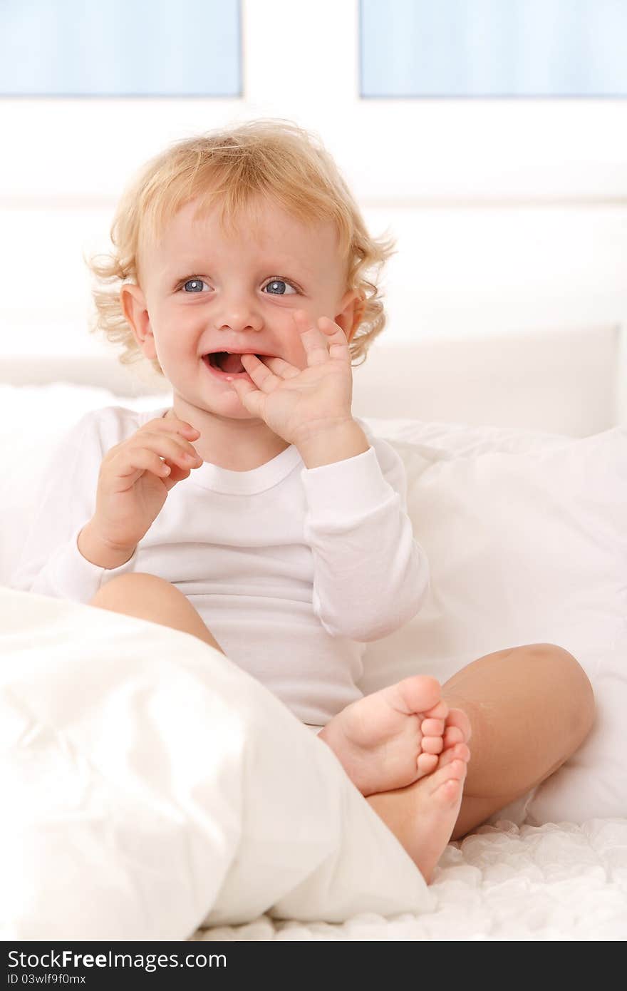 Little boy sitting on a white bed, smiling. Little boy sitting on a white bed, smiling