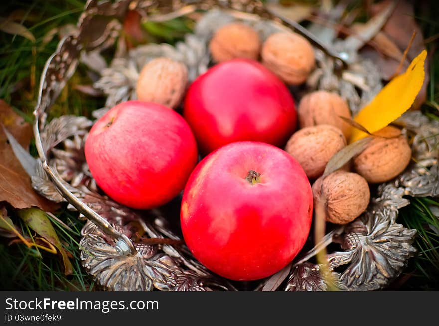 nuts and red apples in the cupronickel basket on the ground. nuts and red apples in the cupronickel basket on the ground