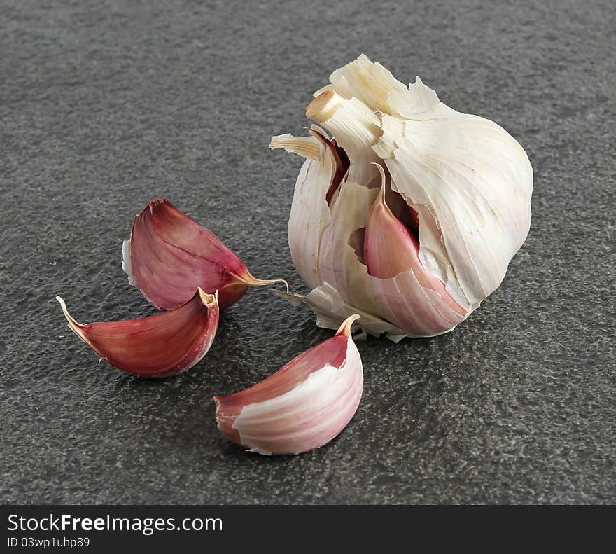 A garlic bulb and three individual cloves on a dark textured background. A garlic bulb and three individual cloves on a dark textured background.