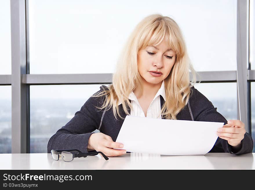 Mid adult woman sitting at a table in the office against the window and work with documants. Mid adult woman sitting at a table in the office against the window and work with documants