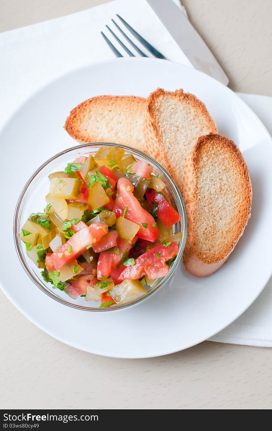 A bowl of salad made of cucumbers and tomatoes and croutons on a white plate.