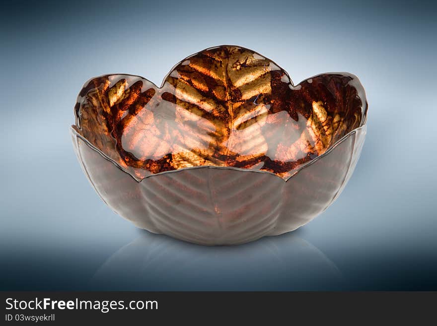 Orange glass vase with leaf like texture against blue reflective background. Orange glass vase with leaf like texture against blue reflective background