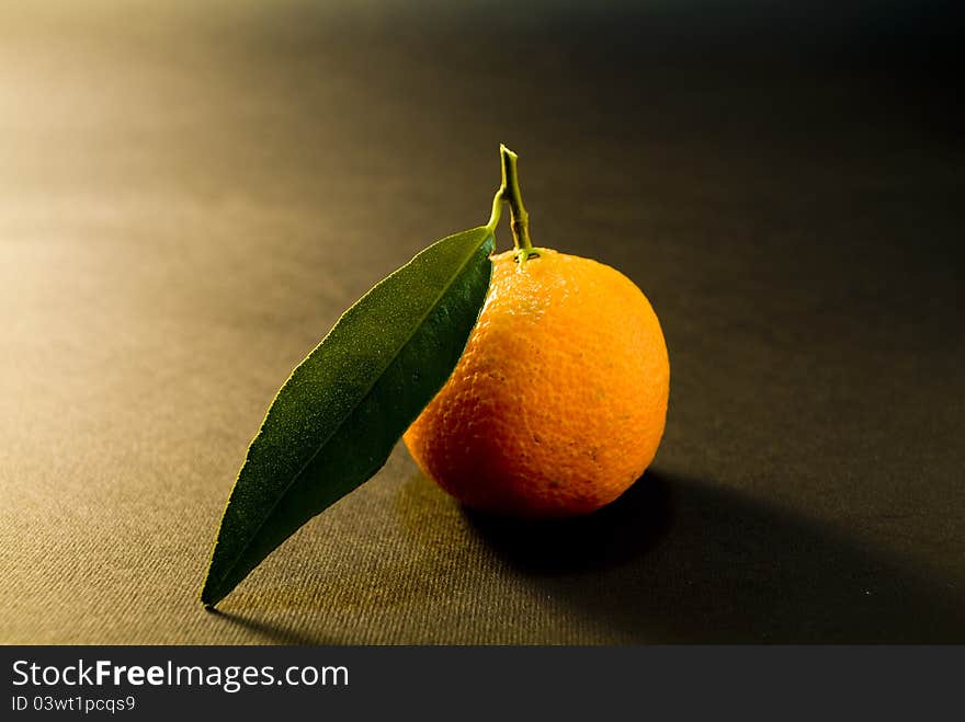 Ripe tangerine with green on a black background. Ripe tangerine with green on a black background