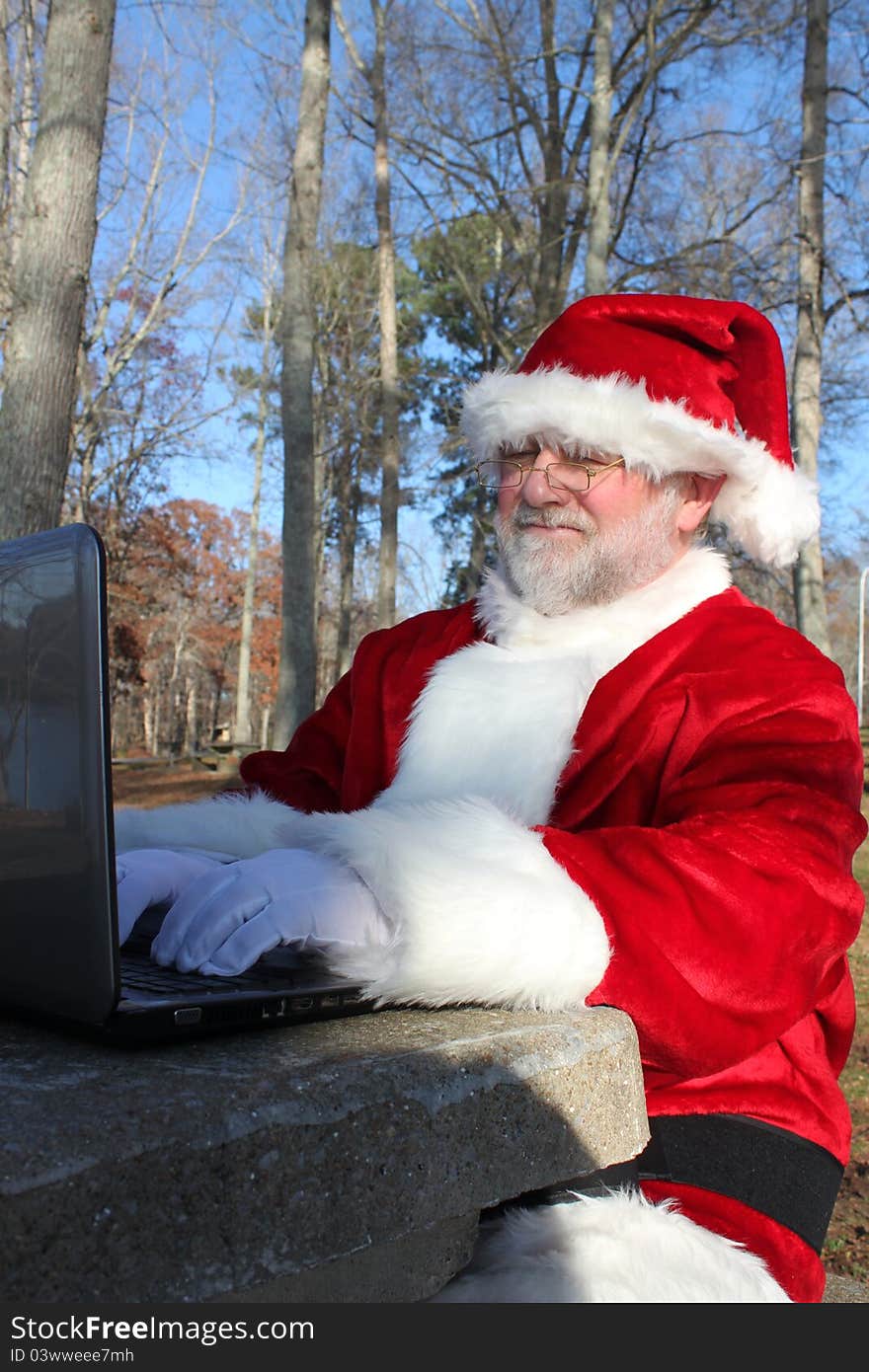 Santa sitting at a park table doing some last minute online shopping on his computer. Santa sitting at a park table doing some last minute online shopping on his computer.