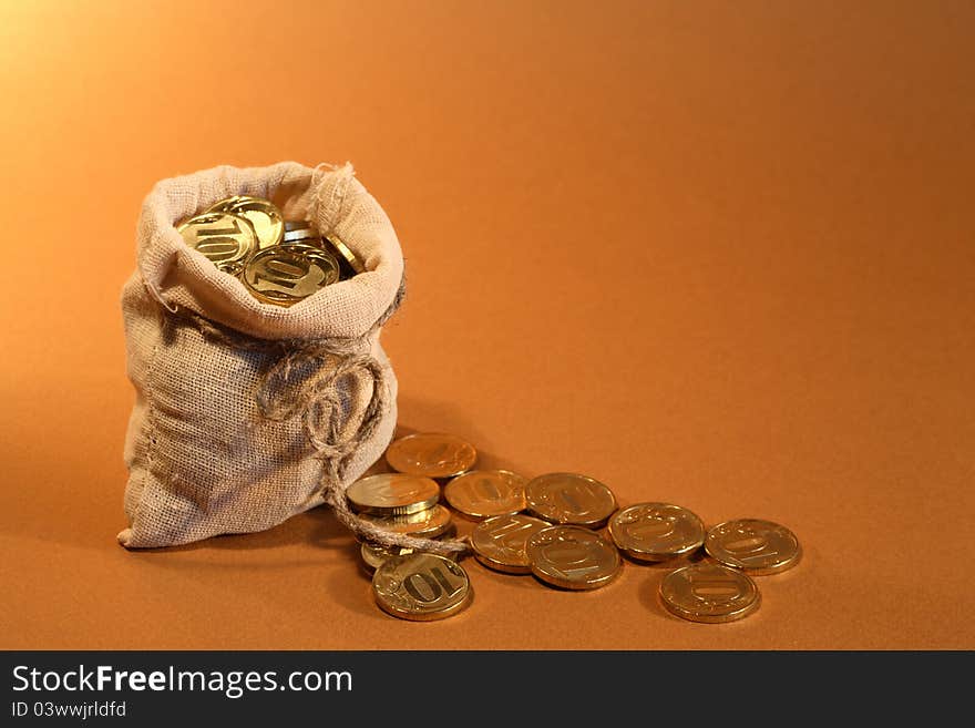 Wealth concept. Open burlap sack full of golden coins standing on orange background. Wealth concept. Open burlap sack full of golden coins standing on orange background