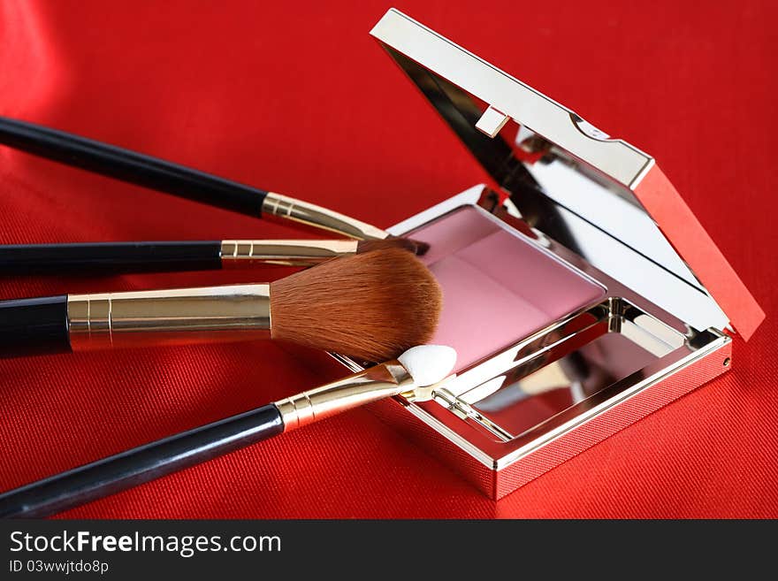 Few makeup brushes and rouge on red silk surface. Few makeup brushes and rouge on red silk surface