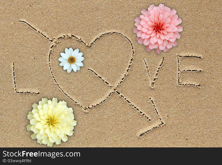 Love word with love symbol and flowers on sand. Love word with love symbol and flowers on sand