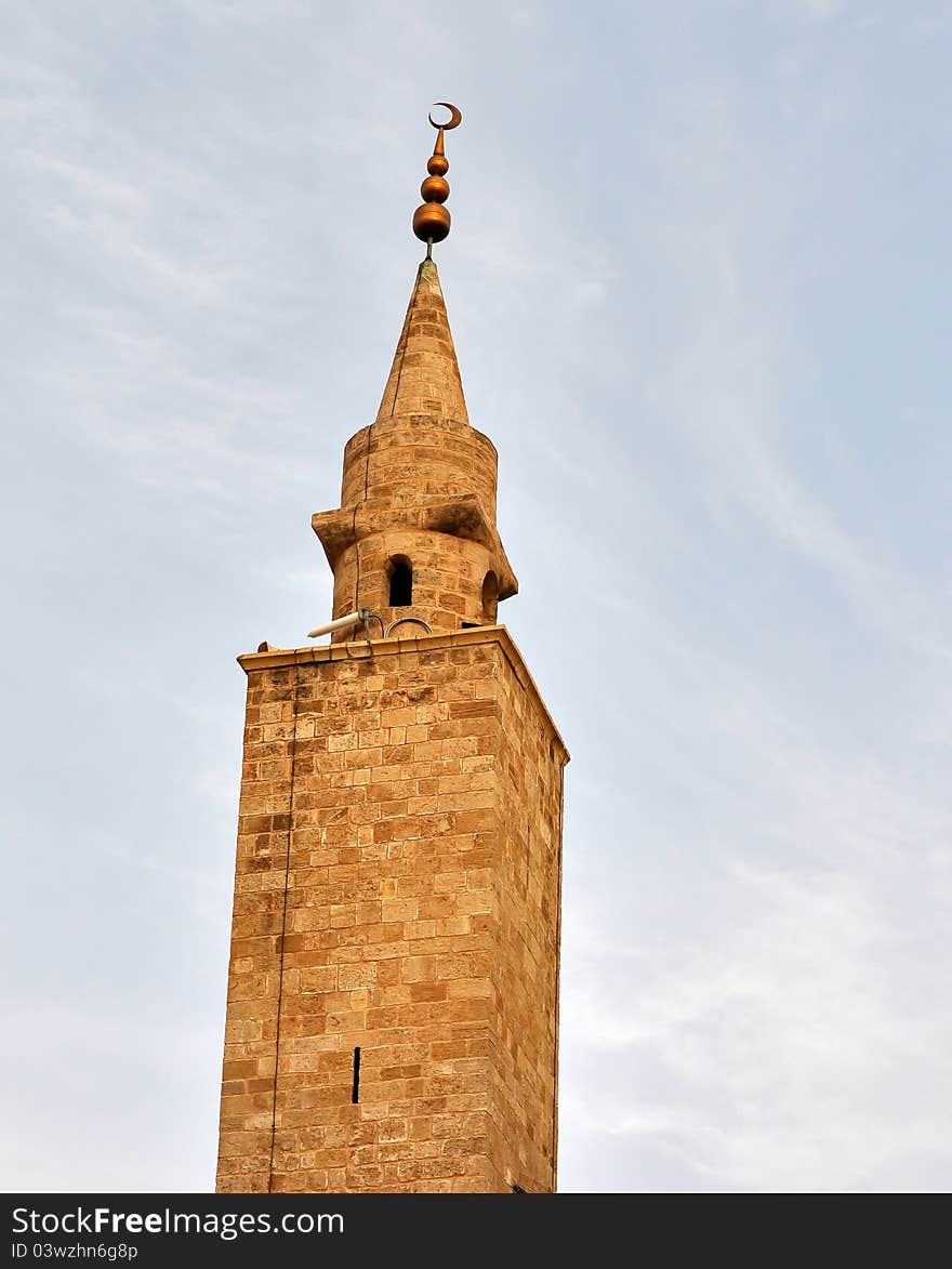 A Mosque minaret made of sand stone with a bronze crescent that tops it. A Mosque minaret made of sand stone with a bronze crescent that tops it