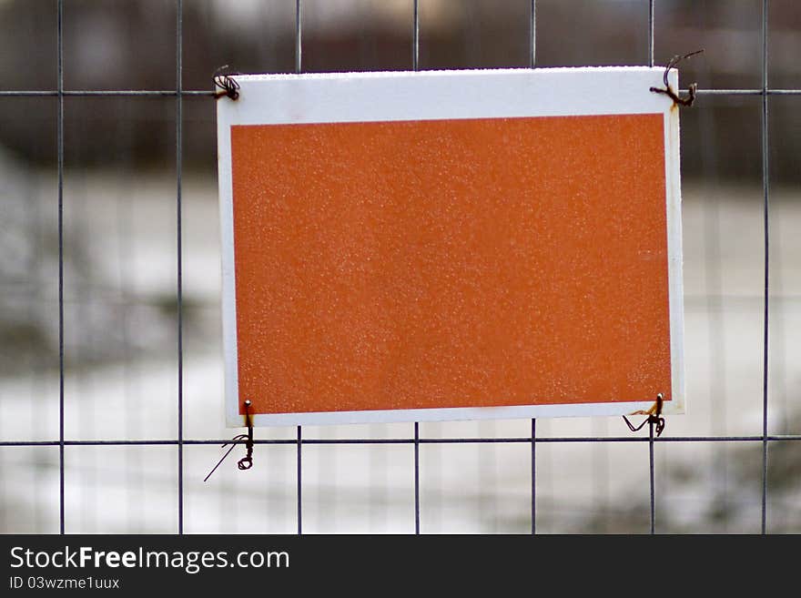 Blank orange sign attached to metal fence. Blank orange sign attached to metal fence.