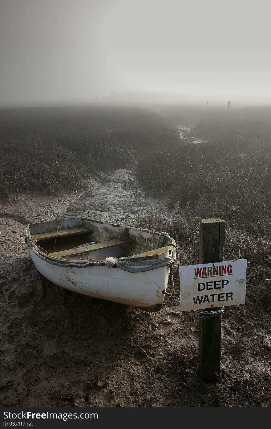 Small boat in mud tied to a sign in the fog. Small boat in mud tied to a sign in the fog