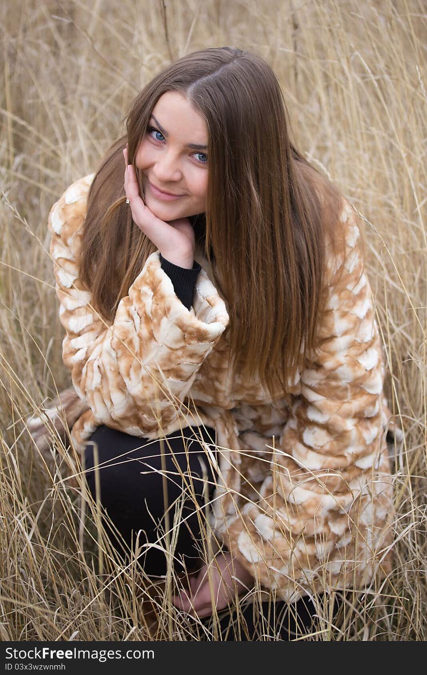 Nice girl in a fur coat sitting on a background of wheat field