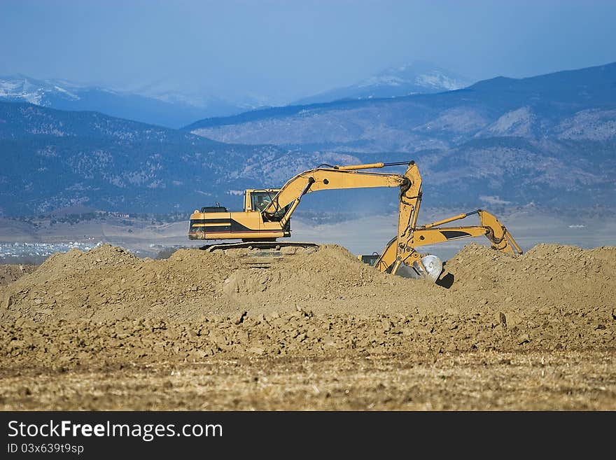 A pair of excavators moves dirt at a construction site. A pair of excavators moves dirt at a construction site.