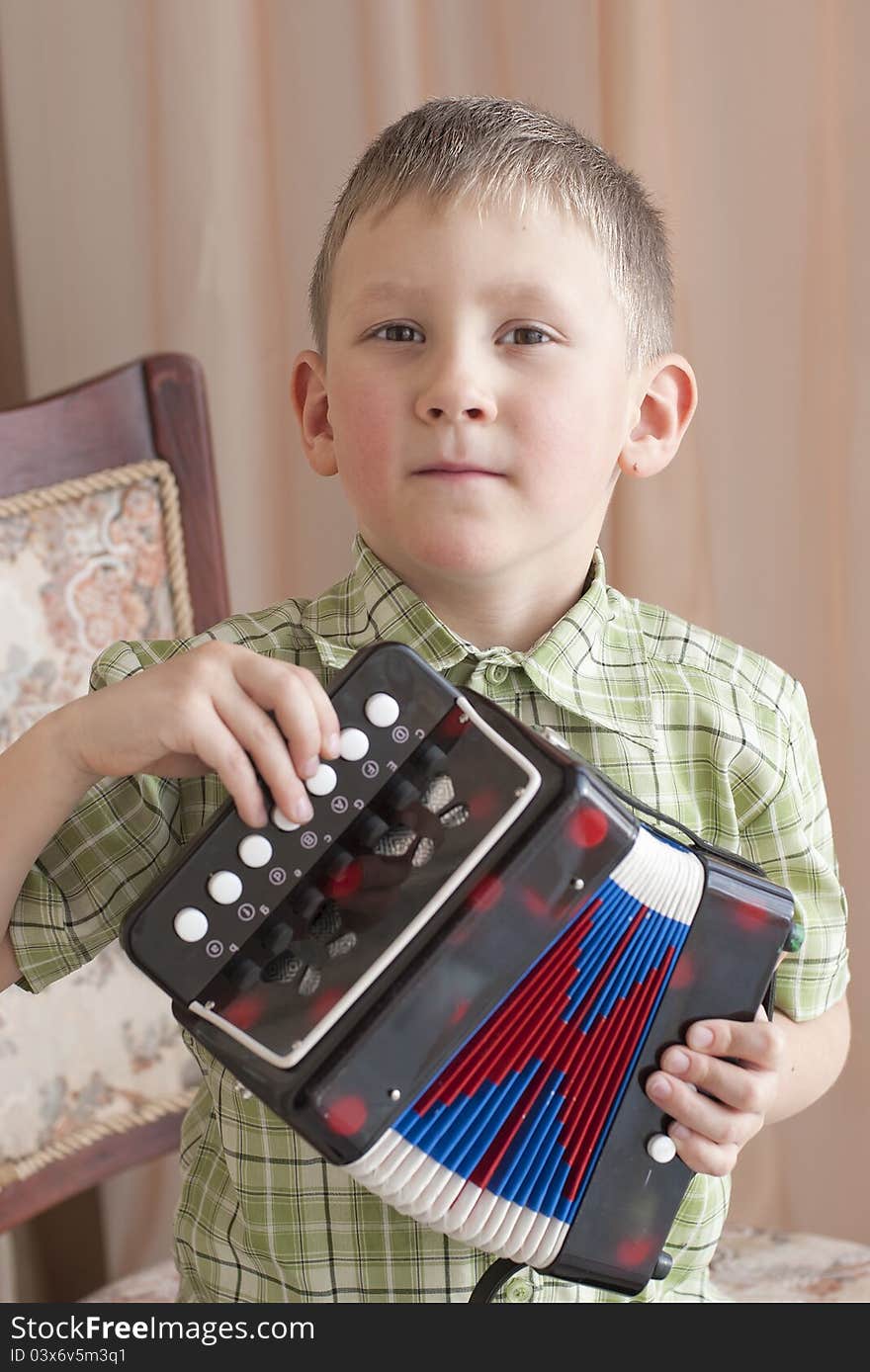 The little boy sits on chair and plays an accordion