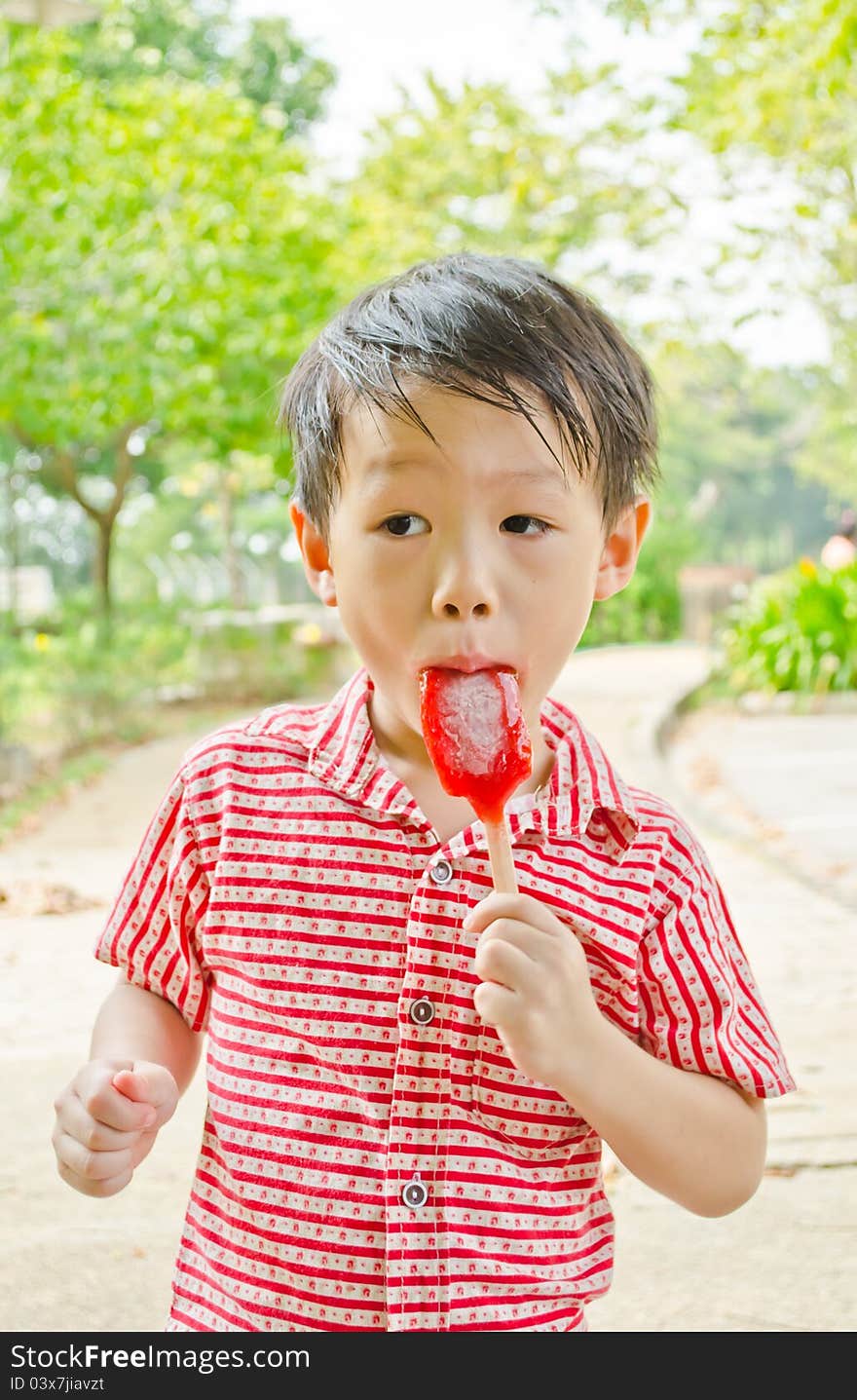 Young asian boy eating fruit flavour ice-cream in park. Young asian boy eating fruit flavour ice-cream in park