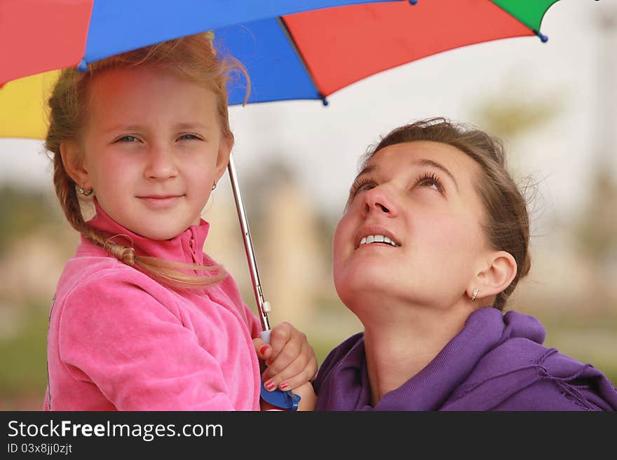 Girl and mom are hiding under the umbrella of color fall. Girl and mom are hiding under the umbrella of color fall