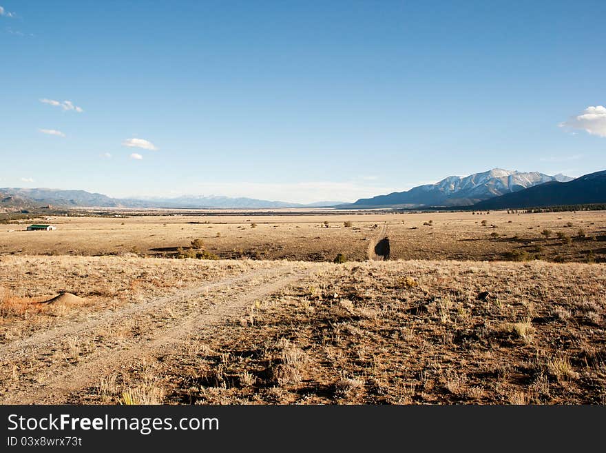 A dry pasture with a dirt road running through it. Mountains lie in the background. A dry pasture with a dirt road running through it. Mountains lie in the background