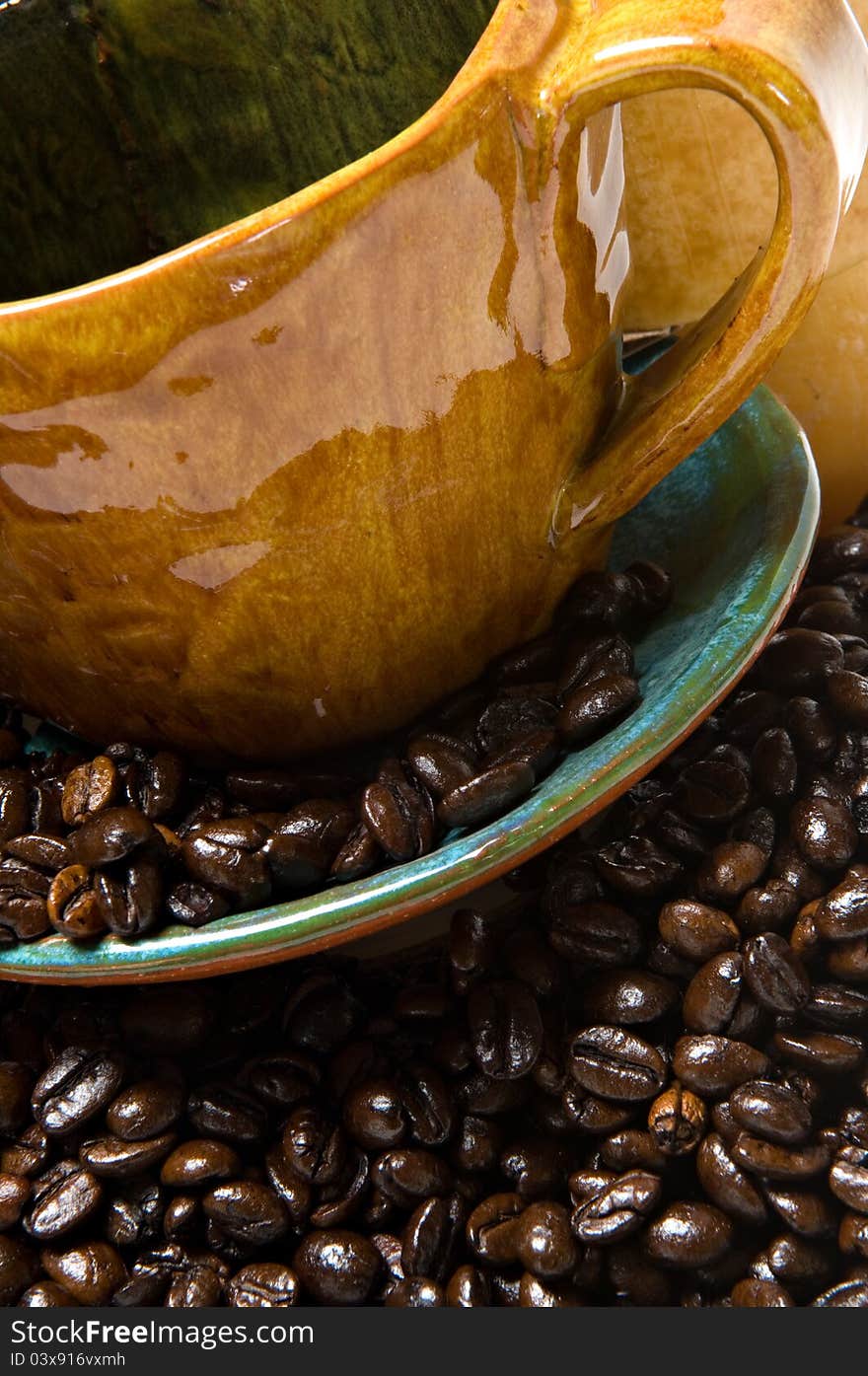 Close up of a coffee mug and saucer overflowing with dark roasted coffee beans.  Shallow depth of field. Close up of a coffee mug and saucer overflowing with dark roasted coffee beans.  Shallow depth of field.