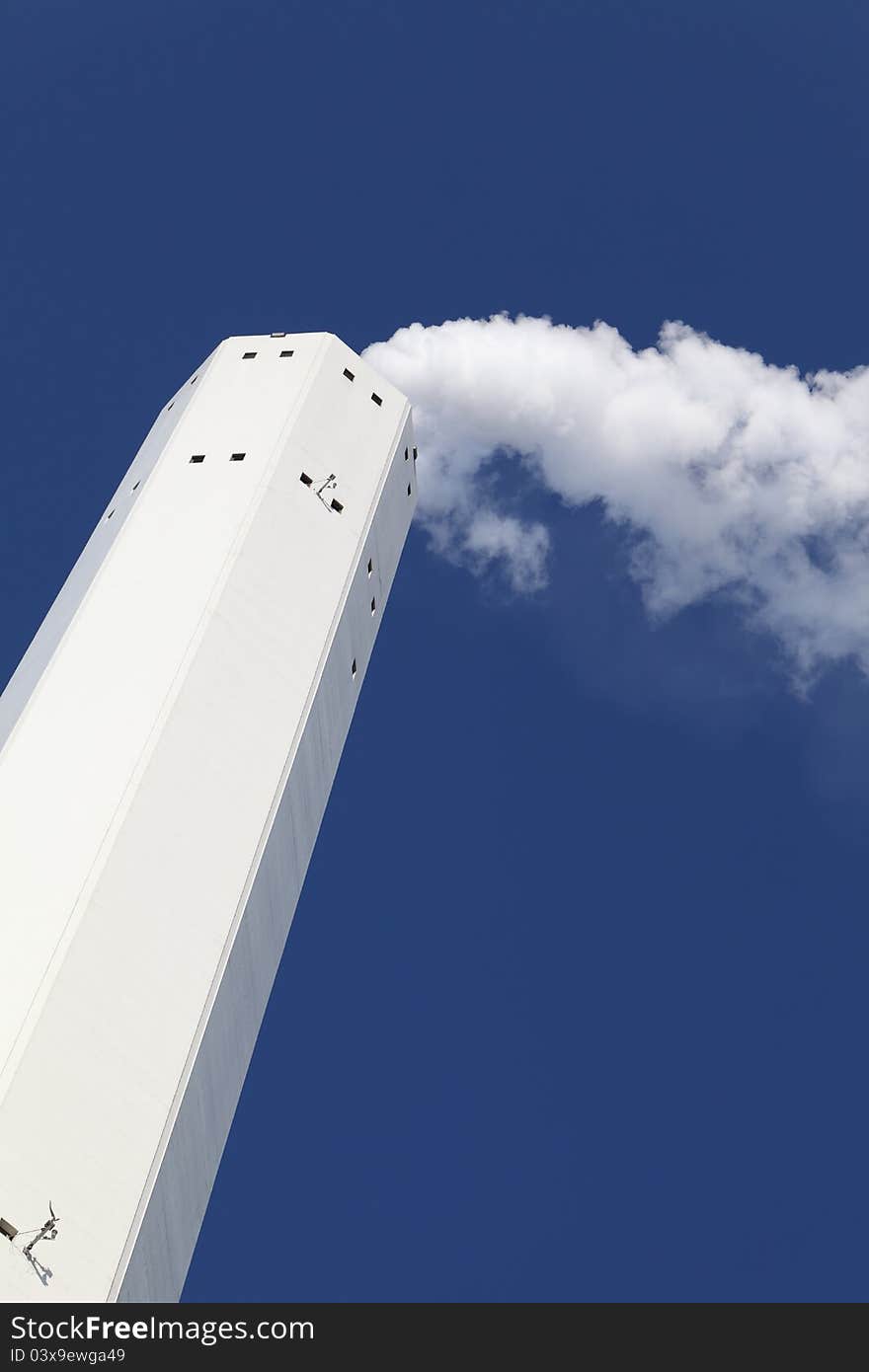 Smokestack with white smoke over blue sky