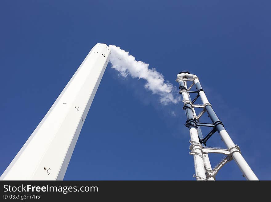 Smokestack with white smoke over blue sky. Smokestack with white smoke over blue sky