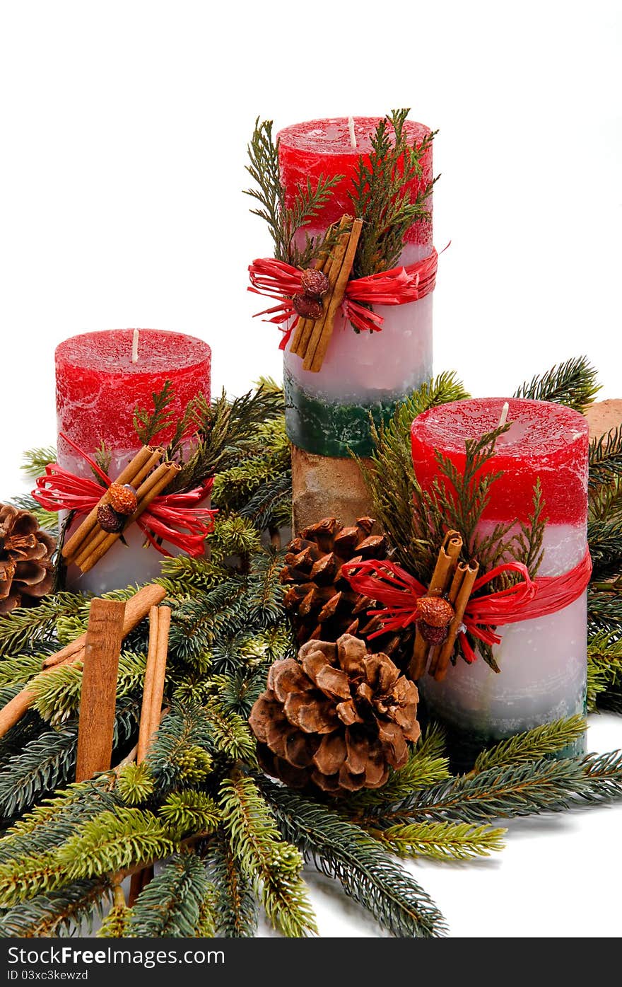 Trio of red, white and green festive candles with green cedar leaves & cinnamon tied on with twine among fresh green pine branches. Trio of red, white and green festive candles with green cedar leaves & cinnamon tied on with twine among fresh green pine branches.