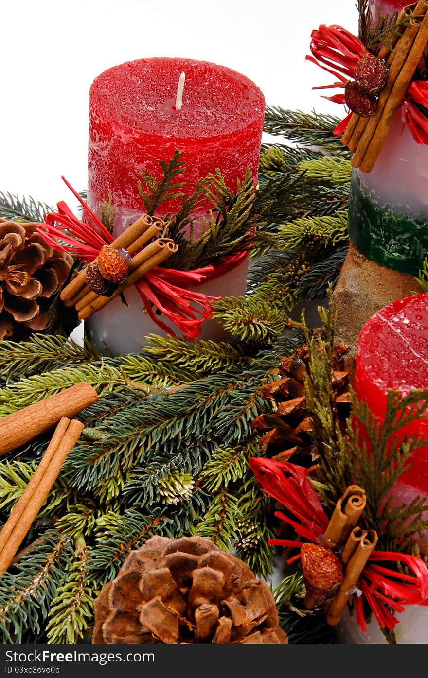 Red festive candles with green cedar leaves & cinnamon tied on with twine among fresh green pine branches. Red festive candles with green cedar leaves & cinnamon tied on with twine among fresh green pine branches.