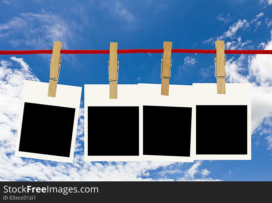 Blank photo frames hang by wooden peg on blue sky