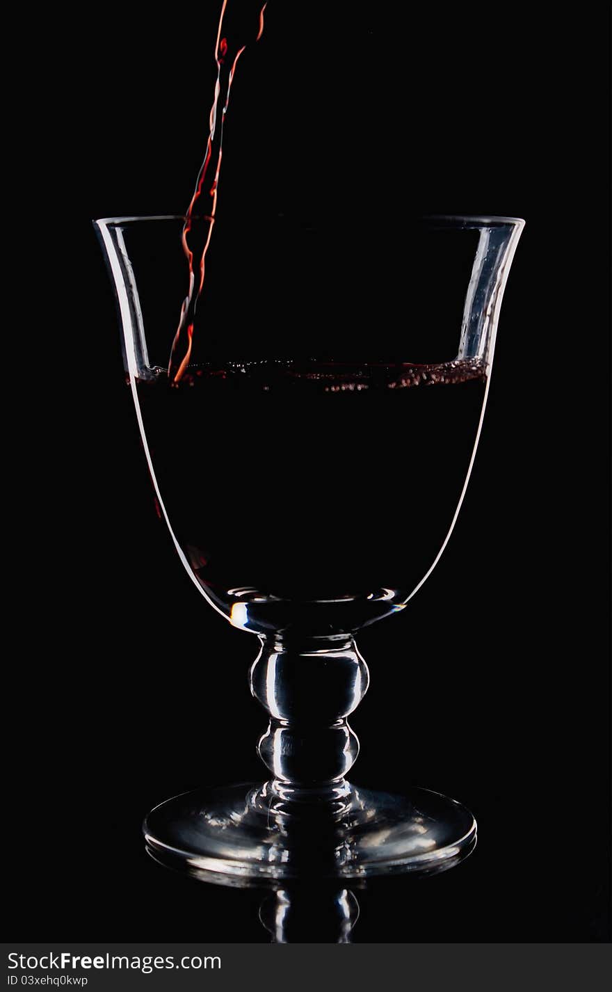 Red wine start to pour in a wineglass,low light photo