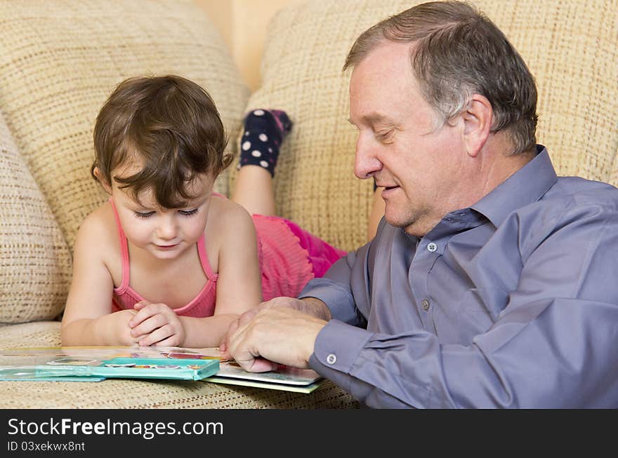 Three years old girl reading and playing with her grandfather. Three years old girl reading and playing with her grandfather.