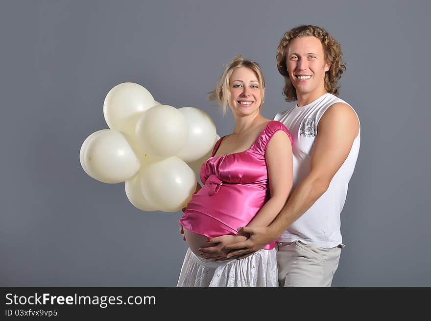 Fashion young couple expecting a baby, gray background with white balloons. Fashion young couple expecting a baby, gray background with white balloons