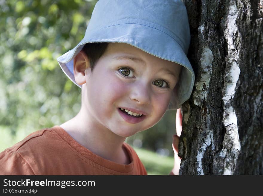 Portrait of an small child boy in a blue sun hat leaning on a birch tree trunk. Portrait of an small child boy in a blue sun hat leaning on a birch tree trunk.