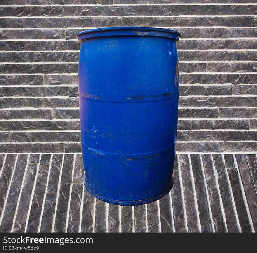 Blue garbage bucket on the stone floor and the stone background.