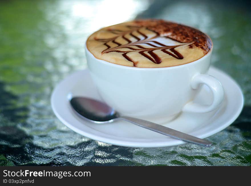 Side view of cappuccino coffee cup with spoon on glass table