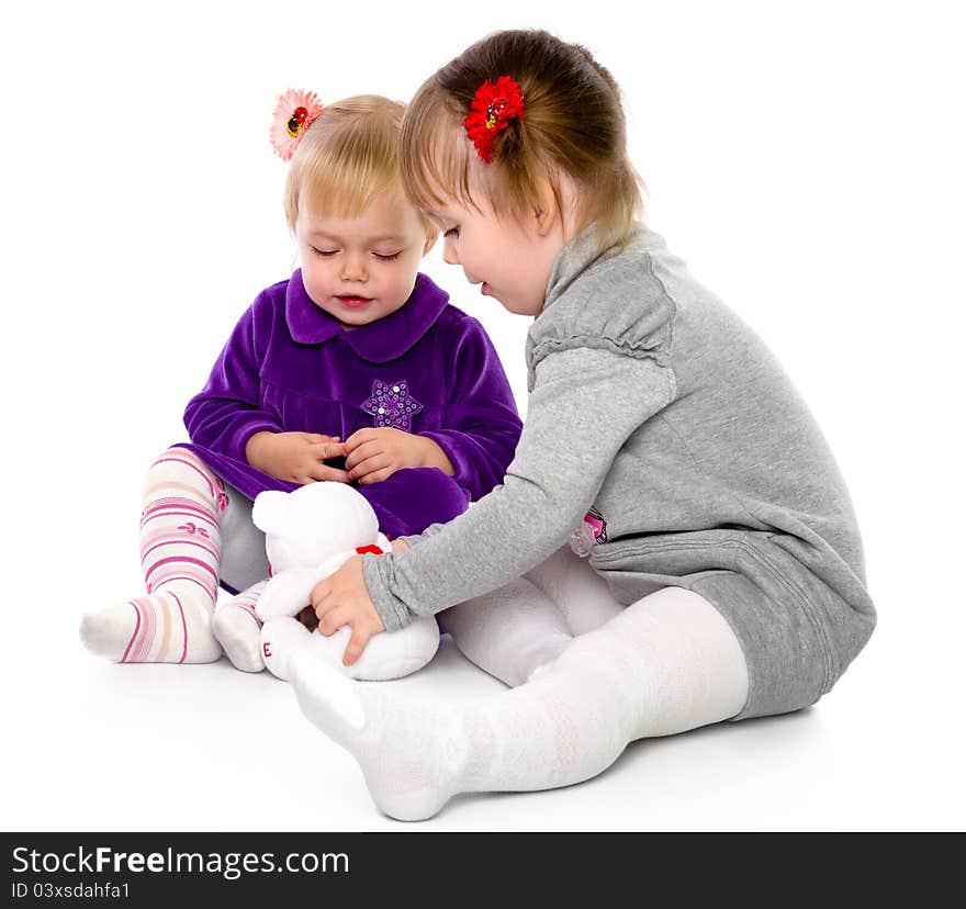 Two girls play with a teddy bear. Isolated on a white background