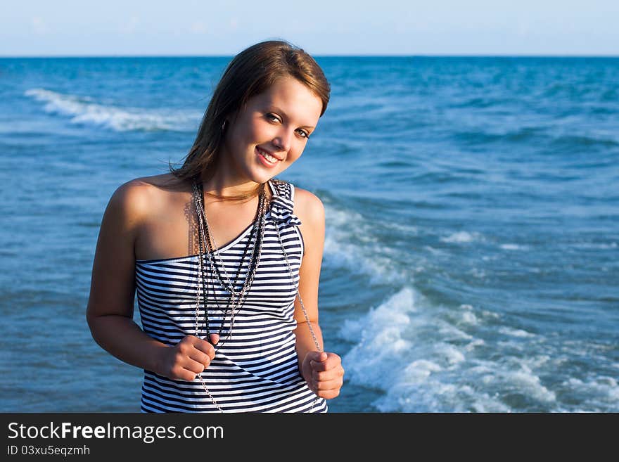 Young pretty girl looking at camers and smiling with the sea as a background. Young pretty girl looking at camers and smiling with the sea as a background