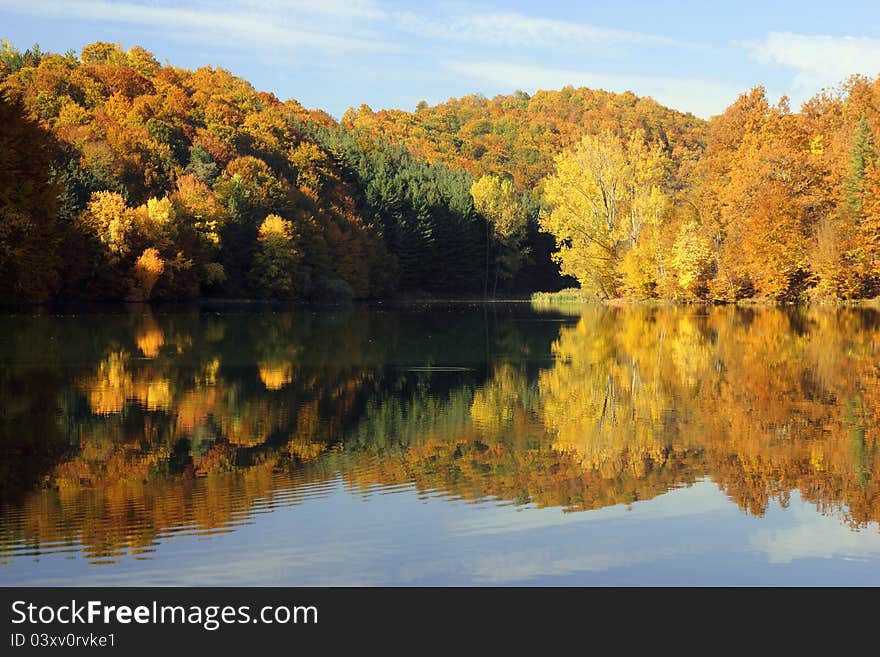 Hills of autumn colors reflected in a calm lake in early morning light