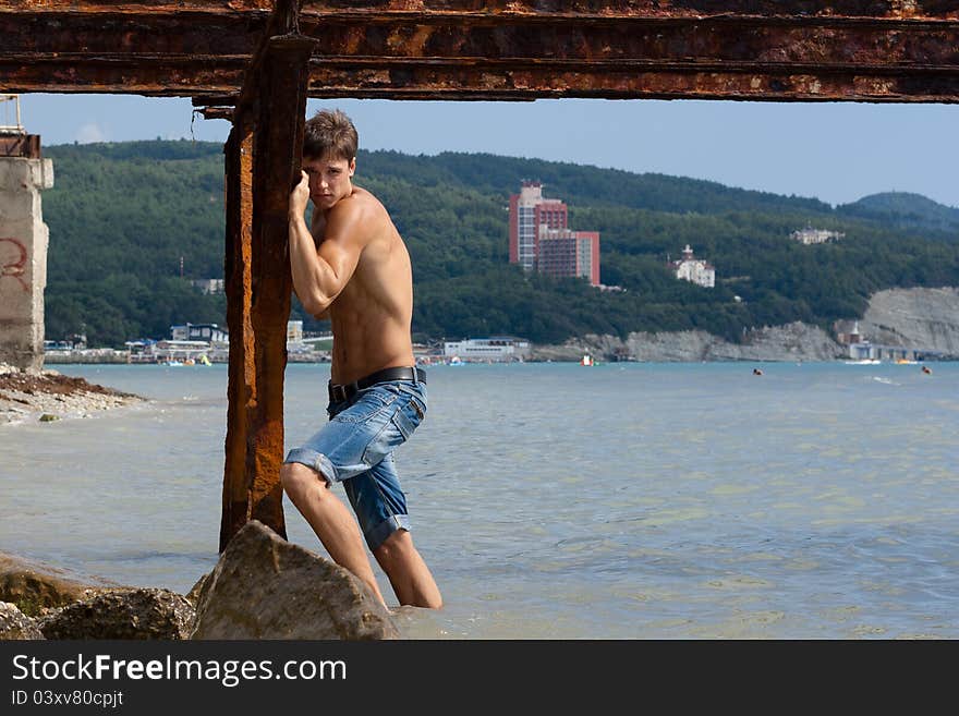 Lad with strong muscles on iron construktion near the sea. Lad with strong muscles on iron construktion near the sea