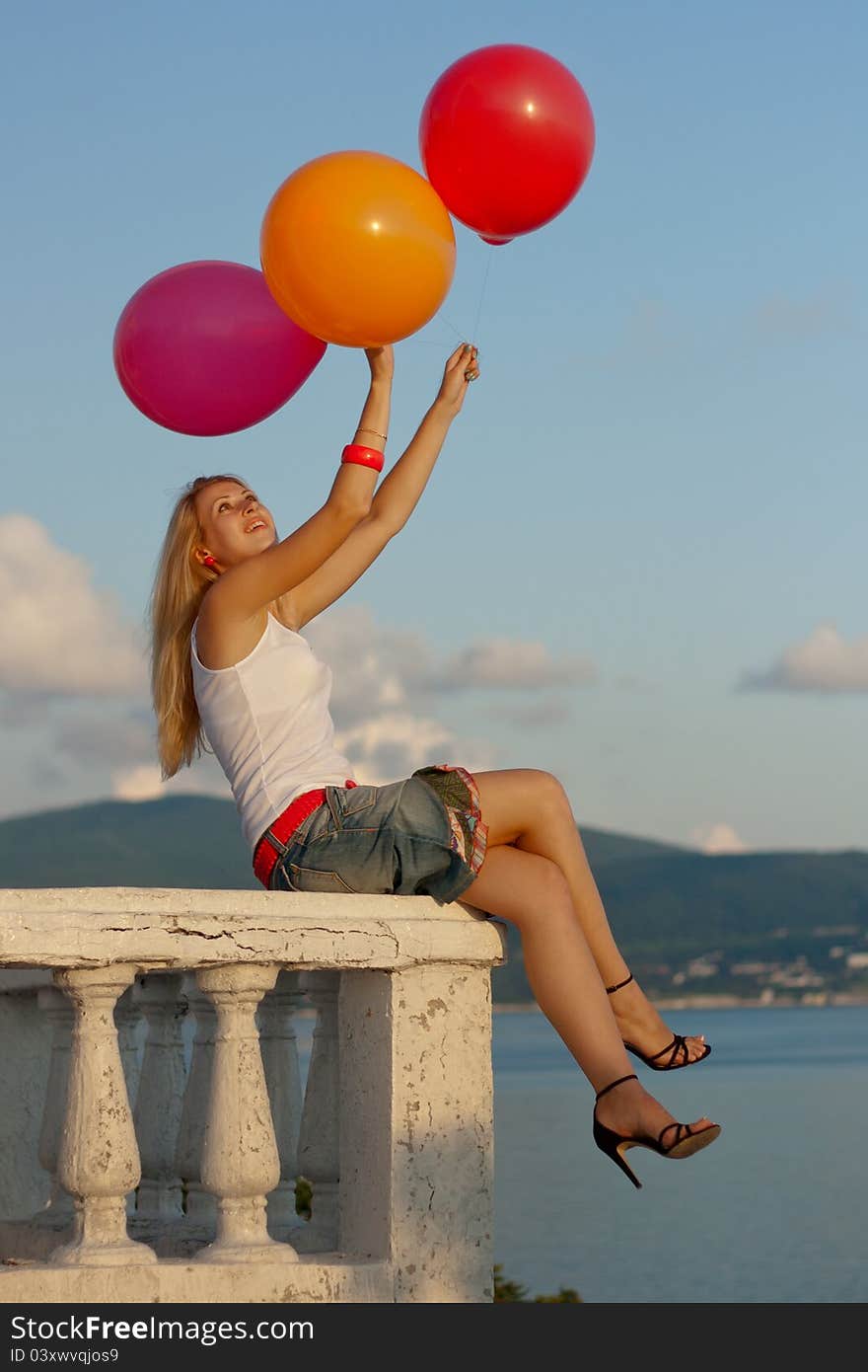 Pretty woman with varicoloured balloons seat on a balcony by the sea