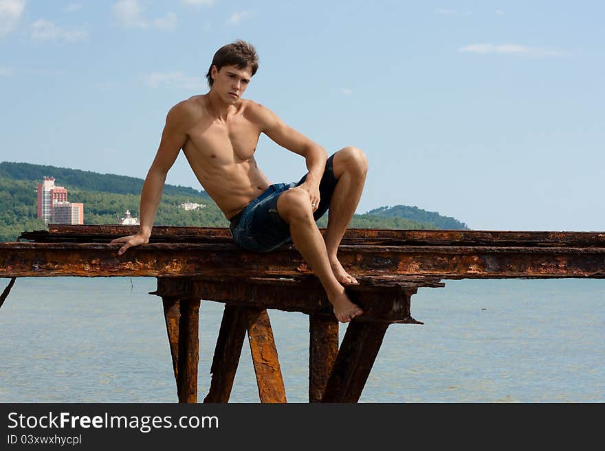 Lad with strong muscles on iron construktion near the sea. Lad with strong muscles on iron construktion near the sea