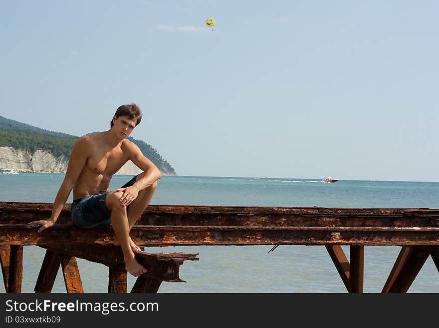 Lad with strong muscles on iron construktion near the sea. Lad with strong muscles on iron construktion near the sea