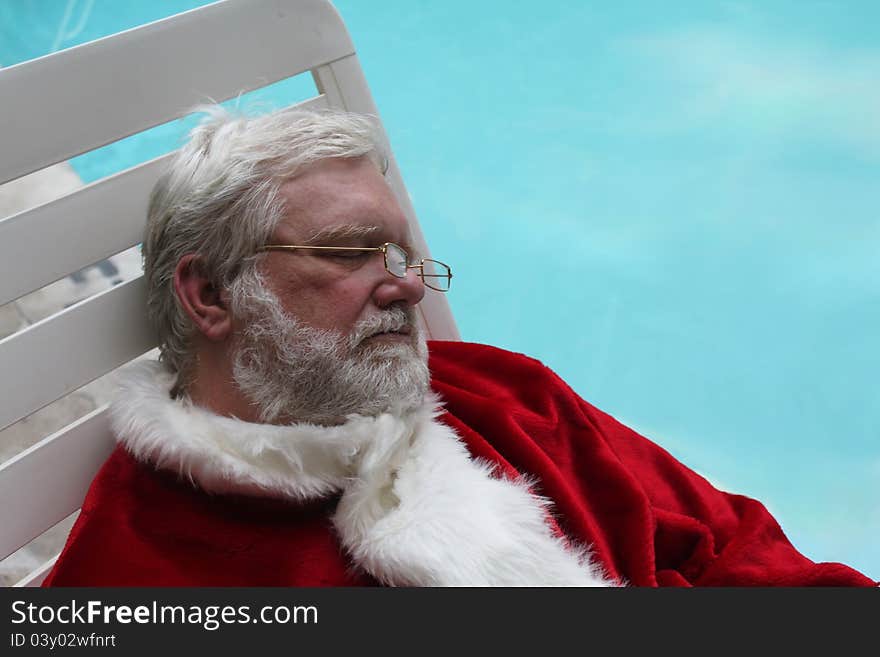 Santa Claus sound asleep on a lounge chair next to a swimming pool. Santa Claus sound asleep on a lounge chair next to a swimming pool.