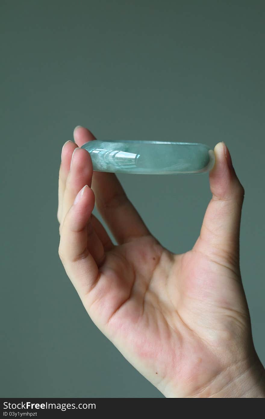 A greenish type A jade / jadeite bracelet holding by female hand towards a grey background. Type A means it has not been treated in any way except surface waxing. A greenish type A jade / jadeite bracelet holding by female hand towards a grey background. Type A means it has not been treated in any way except surface waxing.