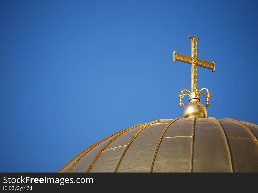 Golden orthodox cross and dome close-up on blue-sky background. Golden orthodox cross and dome close-up on blue-sky background