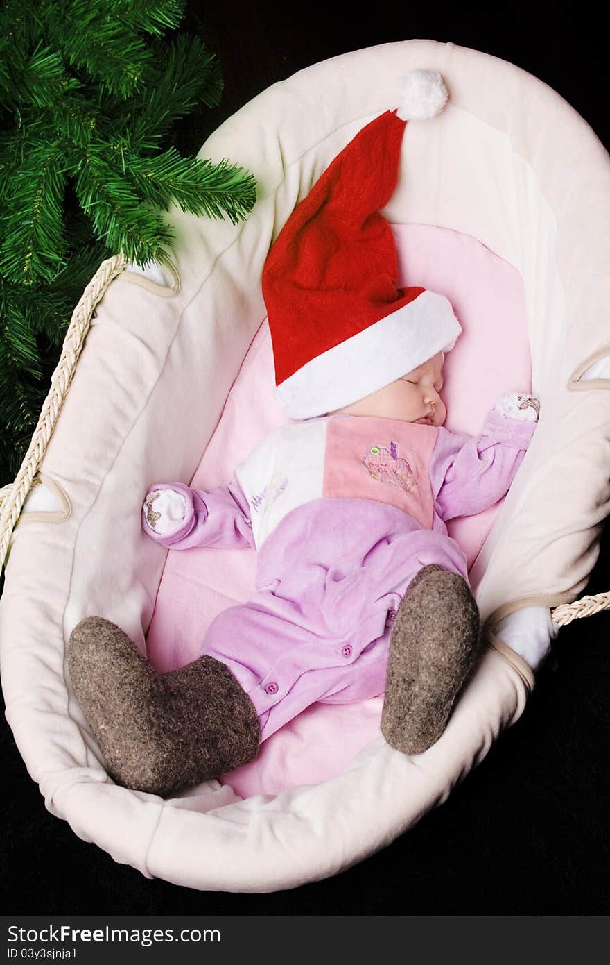 The little baby in winter boots and a hat of Santa Claus sleeps in a basket